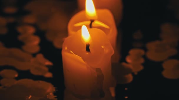 三支石蜡蜡烛在黑色的背景上一排排燃烧 并反射出来 三支白色的蜡烛在黑暗的背景上燃烧着明亮的橙色火焰 悲伤的象征 对死者的纪念 战争的概念 — 图库视频影像