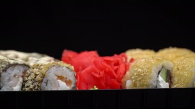 Sushi roll is spinning in a black container close-up. Japanese cuisine sushi in a restaurant. Sushi roll with salmon and vegetables. Japan restaurant menu. Side view.