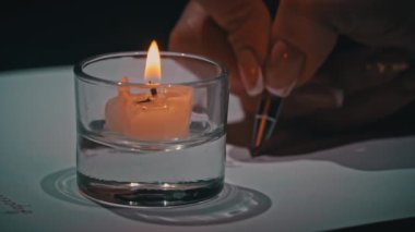 Mans yakın plan beyaz kağıt üzerine antika bir kalem ile el yazısı. Kalem ve mürekkeple beyaz bir kağıda yazı kalemi ve mürekkep yazmış. Mum ışığında büyük harflerle bir mektup yaz..