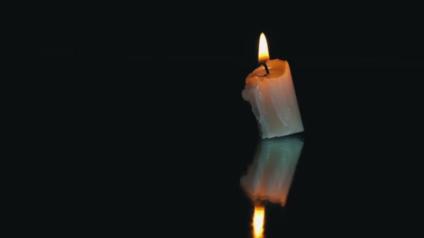 一支短短的石蜡蜡烛在黑色的背景上反射燃烧 一支淡淡的蜡烛在黑暗的背景下燃烧着明亮的橙色火焰 悲伤的象征 对死者的记忆 战争的概念 — 图库视频影像