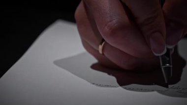 Mans yakın plan beyaz kağıt üzerine antika bir kalem ile el yazısı. Kalem ve mürekkeple beyaz bir kağıda yazı kalemi ve mürekkep yazmış. Mum ışığında büyük harflerle bir mektup yaz..