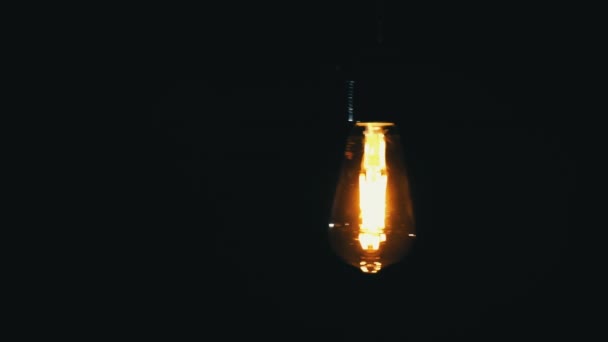 アンティークライトバルブは黒い背景にオレンジ色を燃やします ヴィンテージライトの明るい光が輝いています 白熱ランプはオレンジ色のダークルームを照らします — ストック動画