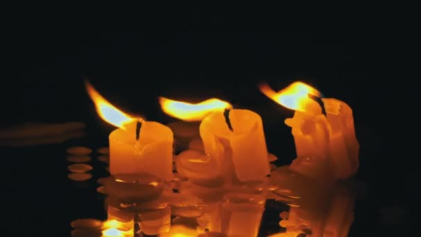 三支石蜡蜡烛在黑色的背景上一排排燃烧 并反射出来 三支白色的蜡烛在黑暗的背景上燃烧着明亮的橙色火焰 悲伤的象征 对死者的纪念 战争的概念 — 图库视频影像