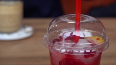 Buzlu, taze ahududu ve limon dilimli uzun bir bardak ahududu limonatası, ahşap bir kafe masasında oturmuş, ferahlatıcı bir mola sunuyor..