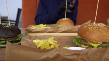 Üç lezzetli burger, ikisi klasik, biri siyah çörekli. Tahta tahtalarda kızarmış patates servis ediliyor. Hamburgerciler için bir ziyafet..