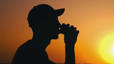 Canlı turuncu bir gün batımına karşı çarpıcı bir siluet. Güneş ufuktan batarken nefes kesen manzaranın tadını çıkararak içkinin tadını çıkarıyor. Uçsuz bucaksız gökyüzü ve yansıtıcı su...