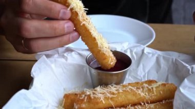 Kızarmış mozzarella çubuğunu domates sosuna batıran biri..