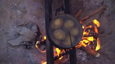 Ateşin üzerinde asılı duran siyah bir su ısıtıcısının içerideki patatesleri gösteren bir fotoğrafı..