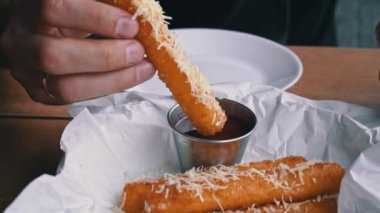 Yakından çekilen bir el, kızarmış mozzarella peynirini kırmızı sos kasesine batırıyor..