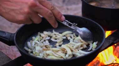 Kavurulmuş soğanları, açık ateşte kızartma tavasında pişiren bir elin görüntülerini kapatın..