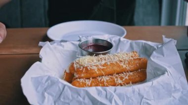 Domates soslu peynirli mozzarella çubuklarının yakın plan çekimi. Çubuklar kağıt bir sepette servis ediliyor ve parmesan peyniri serpiştiriliyor..