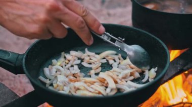 Yakından çekilen fotoğraf, açık ateşte kızarmış soğan karıştıran bir elin resmi..