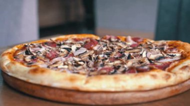 Close-up view of a delicious pizza with mushrooms, salami, bacon, and cheese. The pizza is served on a wooden board.