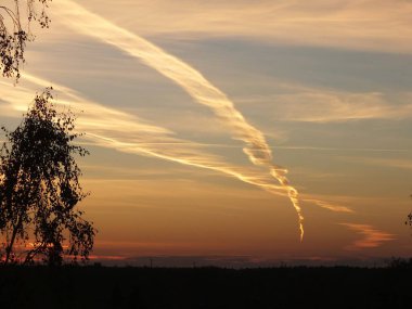 Contrail from a high-altitude flight of a jet airliner at sunset in the sky above Riga's Bolderaja microdistrict. clipart