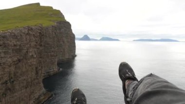 Uçurumdan sarkan erkek bacakları. Faroe Adaları 'ndaki en büyük göl olan Sorvagsvatn Gölü veya Leitisvatn yakınlarında büyük bir dağ veya kaya oluşumu. Okyanusun üzerindeki göl. Bacak Adam Uçurumun kenarında oturuyor.