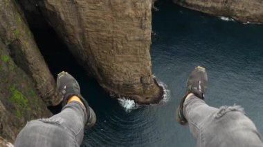 4K Okyanusun üzerindeki Sorvagsvatn Gölü 'nün güzel manzarası ve Vagar, Faroe Adaları' ndaki uçurumdan sarkan insan bacakları. Dikey kaya duvarı. Bacak Adam Uçurumun kenarında oturuyor.