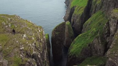 Dunnesdrangar, Faroe Adaları 'na bakan bir adamın 4K hava aracı görüntüsü. İnanılmaz doğa, Faroe Adaları 'ndaki büyük kayalıklar ve dağlar. Vagar Adası. Bir sürü uçan deniz kuşu. Yazın güneşli bir gün.