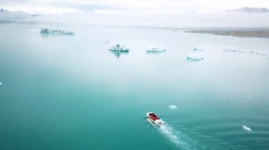 Aerial drone footage of an amphibian boat sailing among icebergs in Jokulsarlon glacier lagoon, Iceland. Scenic view of an Artic nature ice landscape. Melting glacier. Global warming, climate change.