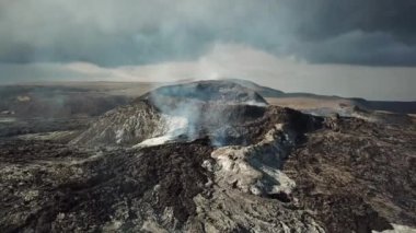 Fagradalsjall 'ın 4K hava aracı görüntüleri Geldingadalir, Reykjanes, İzlanda' da hafif aktif bir volkan patlaması. Duman ve dramatik gökyüzü ile çevrili soğuk lav. İzlanda Volkanik Patlaması Grindavik.