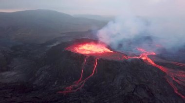 Geldingadalir, Reykjanes, İzlanda 'daki Fagradalsjall volkanik patlamasının 4K hava aracı görüntüleri. Sıcak Lav Nehri dumanla çevrili tepeden aşağı akıyor. İzlanda Volkanik Patlaması Grindavik