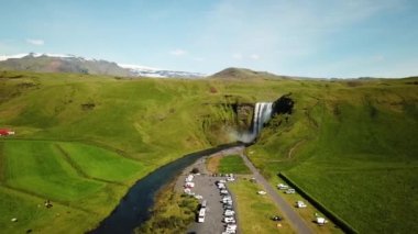İzlanda 'nın güneyindeki bir otoparkta Skogafoss Şelalesi' nin 4K hava aracı görüntüleri. Skogafoss, İzlanda 'nın ünlü şelalesi. Skogafoss 'un manzarası, muhteşem doğal mucize..