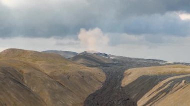 Fagradalsjall 'ın 4K hava aracı görüntüleri Geldingadalir, Reykjanes, İzlanda' da hafif aktif bir volkan patlaması. Duman ve dramatik gökyüzü ile çevrili soğuk lav. İzlanda Volkanik Patlaması Grindavik.