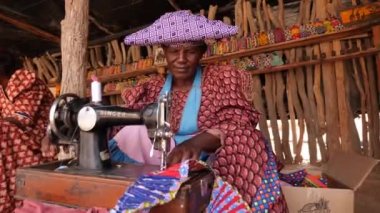 Swakopmund, Namibya - 24 Haziran 23: Renkli Herero kabilesi kadını Namibya, Afrika 'da bir dikiş makinesinde elbise örüyor. Afrika 'daki etnik kabile grubu. Yüksek kalite 4k görüntü