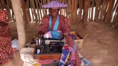 Swakopmund, Namibya - 24 Haziran 23: Renkli Herero kabilesi kadını Namibya, Afrika 'da bir dikiş makinesinde elbise örüyor. Afrika 'daki etnik kabile grubu. Yüksek kalite 4k görüntü