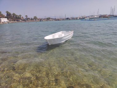 Görüntü, sakin sularda yüzen tek motorlu küçük beyaz bir tekne gösteriyor. Muhtemelen bir körfez ya da göl. Tekne bir rıhtıma ya da bir limana bağlı.