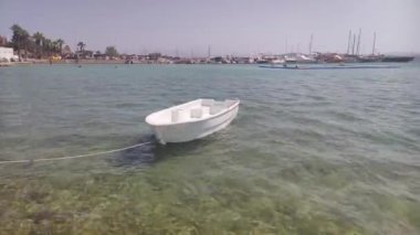 Görüntü, sakin sularda yüzen tek motorlu küçük beyaz bir tekne gösteriyor. Muhtemelen bir körfez ya da göl. Tekne bir rıhtıma ya da bir limana bağlı.
