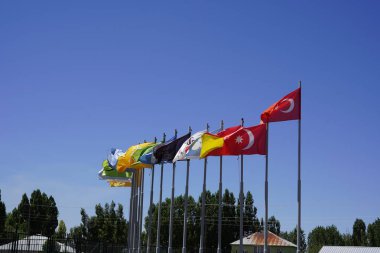 Derin mavi gökyüzü altında 16 Türk devletinin bayrakları: Büyük Türk Bayrağı, Birlik ve Çeşitliliğinin arkasında 16 Türk devletinin bayrakları