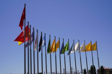 Derin mavi gökyüzü altında 16 Türk devletinin bayrakları: Büyük Türk Bayrağı, Birlik ve Çeşitliliğinin arkasında 16 Türk devletinin bayrakları