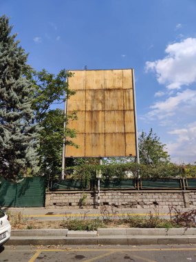 Yaşlanan Billboard Unutulan İletileri Sembolize Ediyor: Yeşillik ve Mavi Gökyüzü Ortasında Hava Durumu, Zamanın Geçişini Yansıtıyor ve İhmal Ediyor.