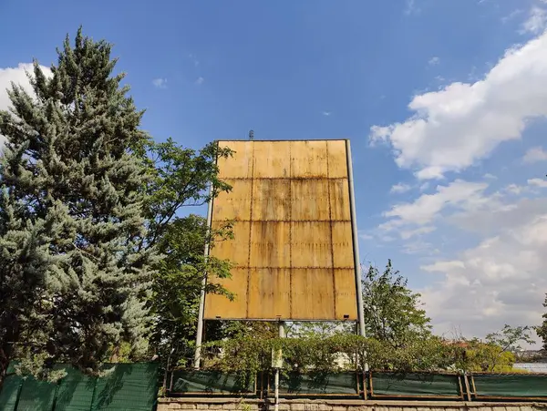 stock image Aging Billboard Symbolizing Forgotten Messages: Weathered Signboard Amid Greenery and Blue Skies, Reflecting the Passage of Time and Neglect.