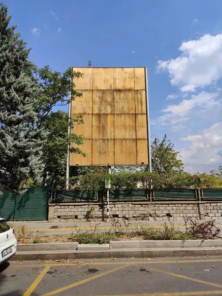 Stock image Aging Billboard Symbolizing Forgotten Messages: Weathered Signboard Amid Greenery and Blue Skies, Reflecting the Passage of Time and Neglect.