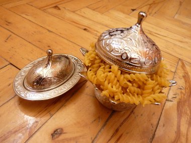 A delicate silver bowl filled with spiral pasta, merging culinary simplicity with ornate elegance, set on a polished wooden surface. The juxtaposition reflects the harmony between tradition. clipart