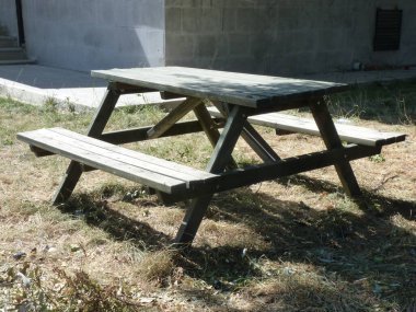 Kuru otların üzerinde güneşli, ahşap bir piknik masası, şehir ortamında yalnızlığı ve sadeliği simgeliyor..
