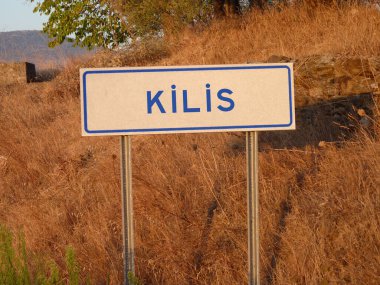 Metal Kutbu 'ndaki Mavi' Kilis 'Tabelası: Kahverengi Çimen ve Yumuşak Gölgelerin Doğal Manzarasına Karşı Kalın Bir Zıtlık, Şehrin Kalbinde Serene Öğleden Sonra Yakalıyor.