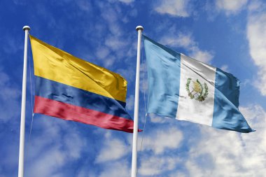 Kolombiya ve Guatemala bayrakları parlak mavi gökyüzüne karşı gururla el sallıyor, güçlü uluslararası bağları, kültürel değişimi ve küresel işbirliğini simgeliyor..