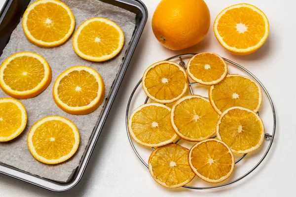 Dry orange slices on metal grill. Fresh orange slices on baking tray. Flat lay. White background.