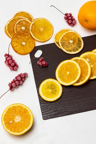 Fresh orange slices on brown board. Sprigs of red frozen berries and dry orange slices on table. Flat lay. White background.