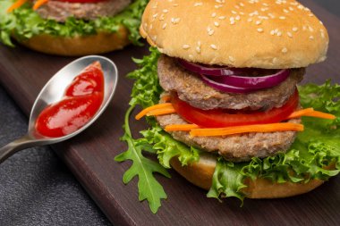 Yeşillikli sığır burger, doğranmış soğan ve havuç. Kasede domates sosu. Kapatın. Siyah arkaplan.