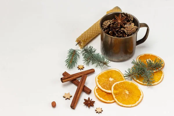 Christmas decorations. Cones in metal mug, candle, cinnamon sticks, sprigs of spruce and dry orange slices. Copy space. White background.