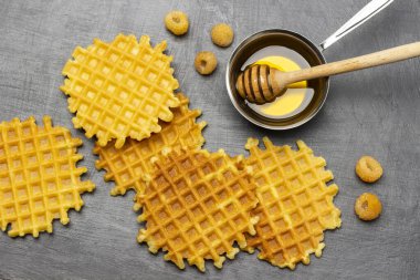 Masada sarı ahududu ve çıtır waffle var. Ballı şeker kâsesinde. Düz yatıyordu. Gri arkaplan.