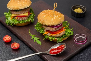 İki yeşil etli burger, doğranmış soğan ve havuç. Kaşıkta domates sosu. Siyah arkaplan.