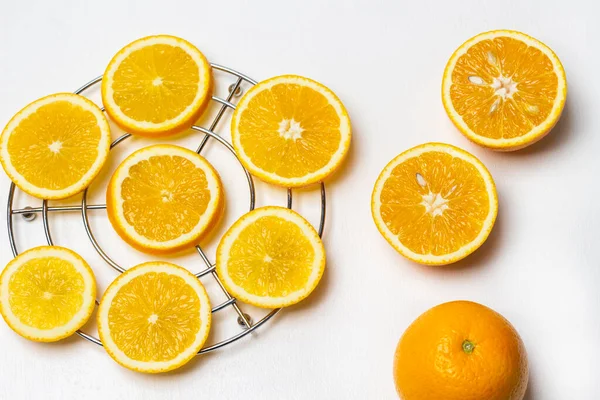 Sliced orange slices on a metal stand. Two halves and a whole orange. Flat lay. White background.