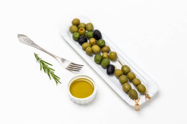 Green olives on a white plate. Olive oil in a bowl, fork on the table. Top view.  White background.