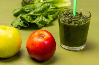Red and green apple. Glass with mixed vegetables. Lettuce leaves. Top view. Green background.