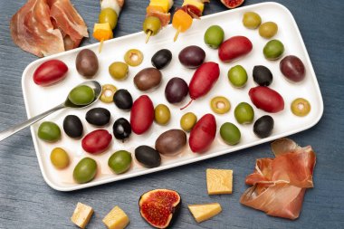 Olives of different varieties and colors a white plate. Cheese, olives, jamon and figs on a table. Flat lay. Blue background.