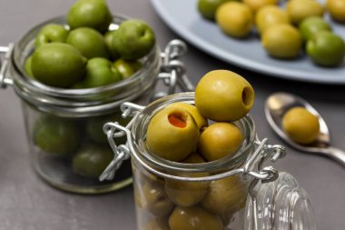 Green olives in glass jars. Olives on a blue plate. Close up. Grey background.